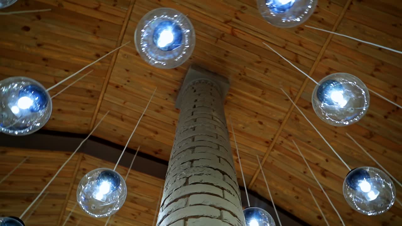 Modern ceiling with light lamp balls. Many round light balls hanging around brick column in the hall. Beautiful glass bulbs on brown background.