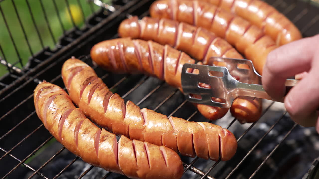 Hot tasty sausages on grill. Cook turning over almost ready sausages for the picnic. Frying food on charcoals in the garden. Close-up.