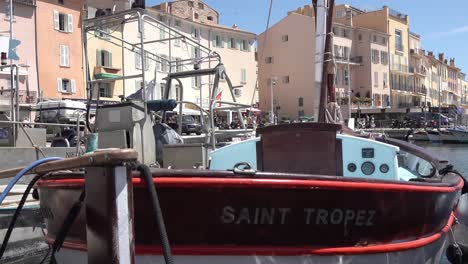 Antiguo-Puerto-De-Saint-tropez-Con-Un-Barco-Pesquero-En-Primer-Plano-Y-Restaurantes-Al-Fondo