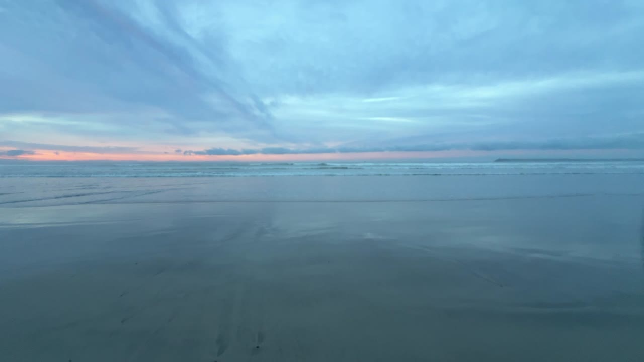 Static wide shot of ocean waves during sunset with pastel sky