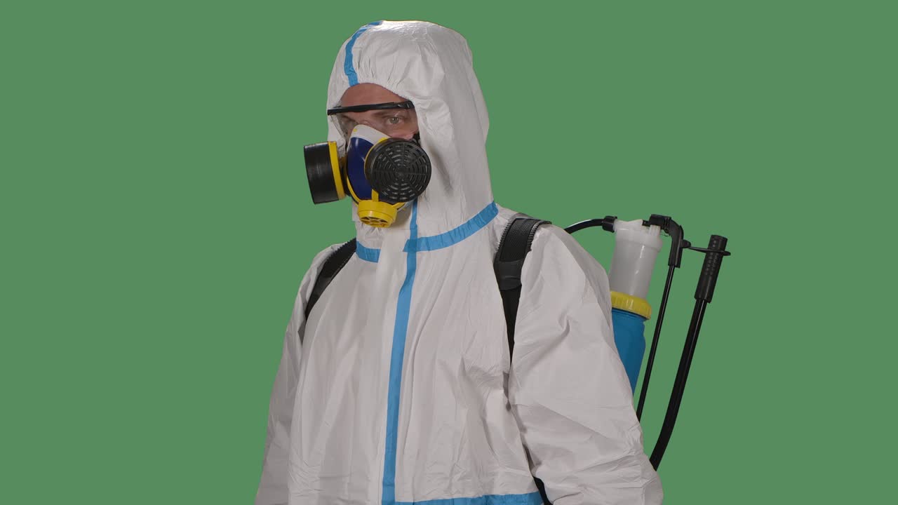 retrato de un hombre con un traje de protección, gafas de seguridad, guantes y un respirador mira con confianza a la cámara y luego dobla los brazos delante de él. pantalla verde, llave de croma. cámara lenta. primer plano