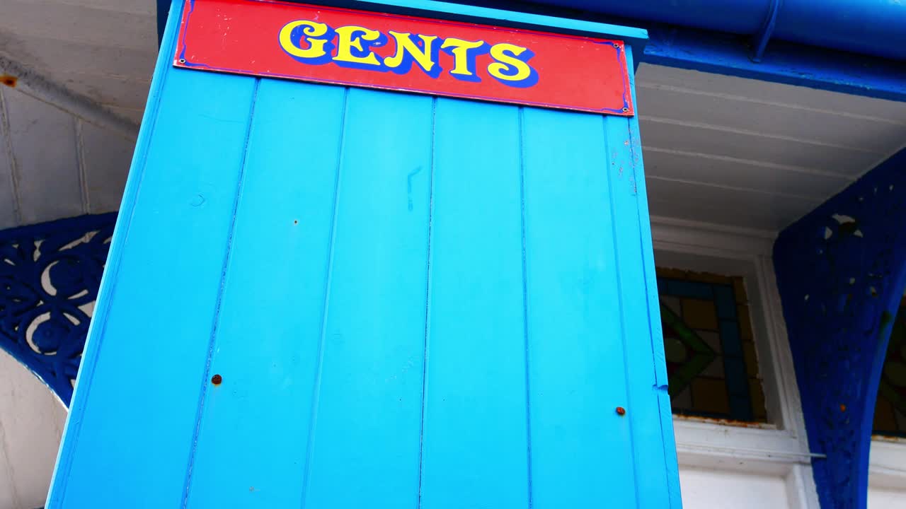 Colourful blue vintage wooden gentleman's toilet door low angle on seaside promenade dolly right