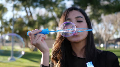 una hermosa chica hispana soplando muchas burbujas de ensueño coloridas flotando al aire libre bajo el sol en cámara lenta