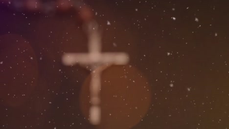composite video of white particles falling over spots of light and close up of rosary