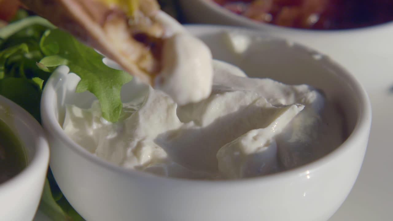 Nærbillede af mad, der dyppes i cremet hvid sauce.
