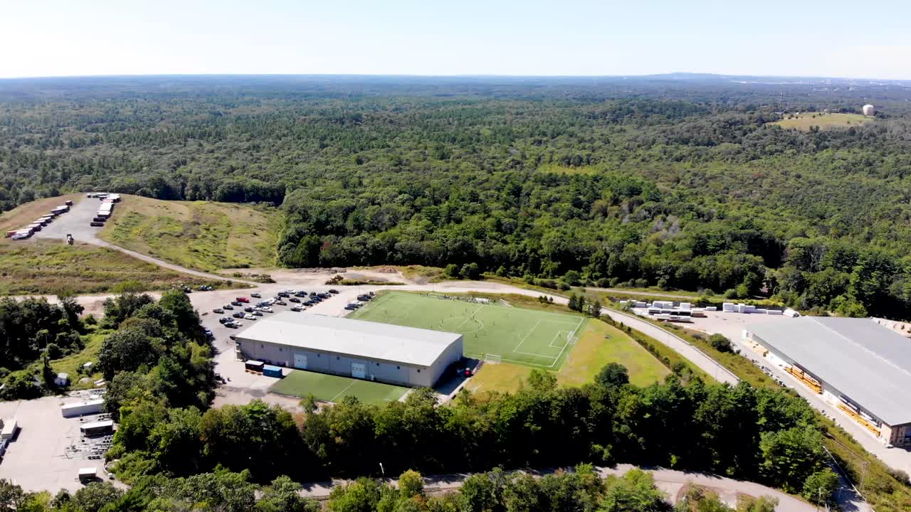 una vista fija de un dron de un campo de fútbol y una instalación deportiva que da a un bosque exuberante y extenso