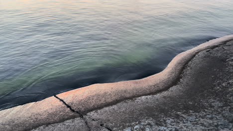 Small-waves-hitting-rock-shore-during-sunset-creating-peaceful-atmosphere