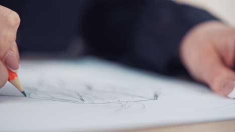 woman's hand with a beautiful ring of a designer is drawing sketch of dress in atelier. female tailor draws with a sharp pencil on the table. close-up