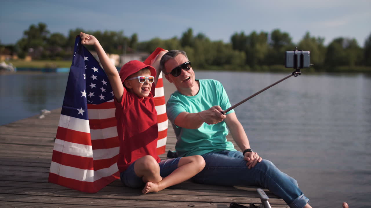 Father and Son Take a Selfie with the American Flag on a Lake Pier