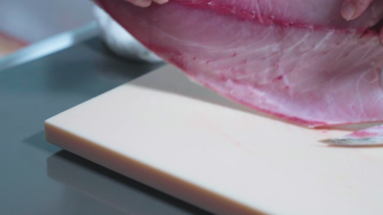 A sliding shot of a skinned fish being carefully flipped to its other side, demonstrating the precision and technique involved in fish preparation for cooking or further processing.