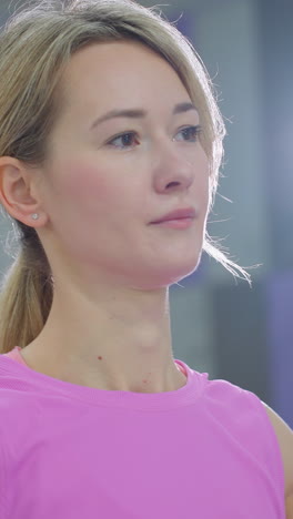 primer plano de una mujer con ropa deportiva rosa realizando un estiramiento en un estudio de fitness, brazos extendidos mientras se mueve de izquierda a derecha, luz recta en el fondo