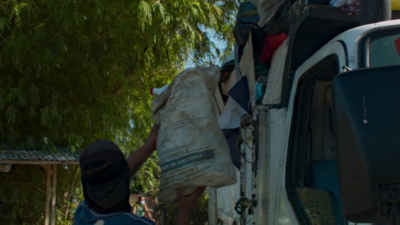 Garbage collector hands sack of rubbish to coworker who carries it with one hand.