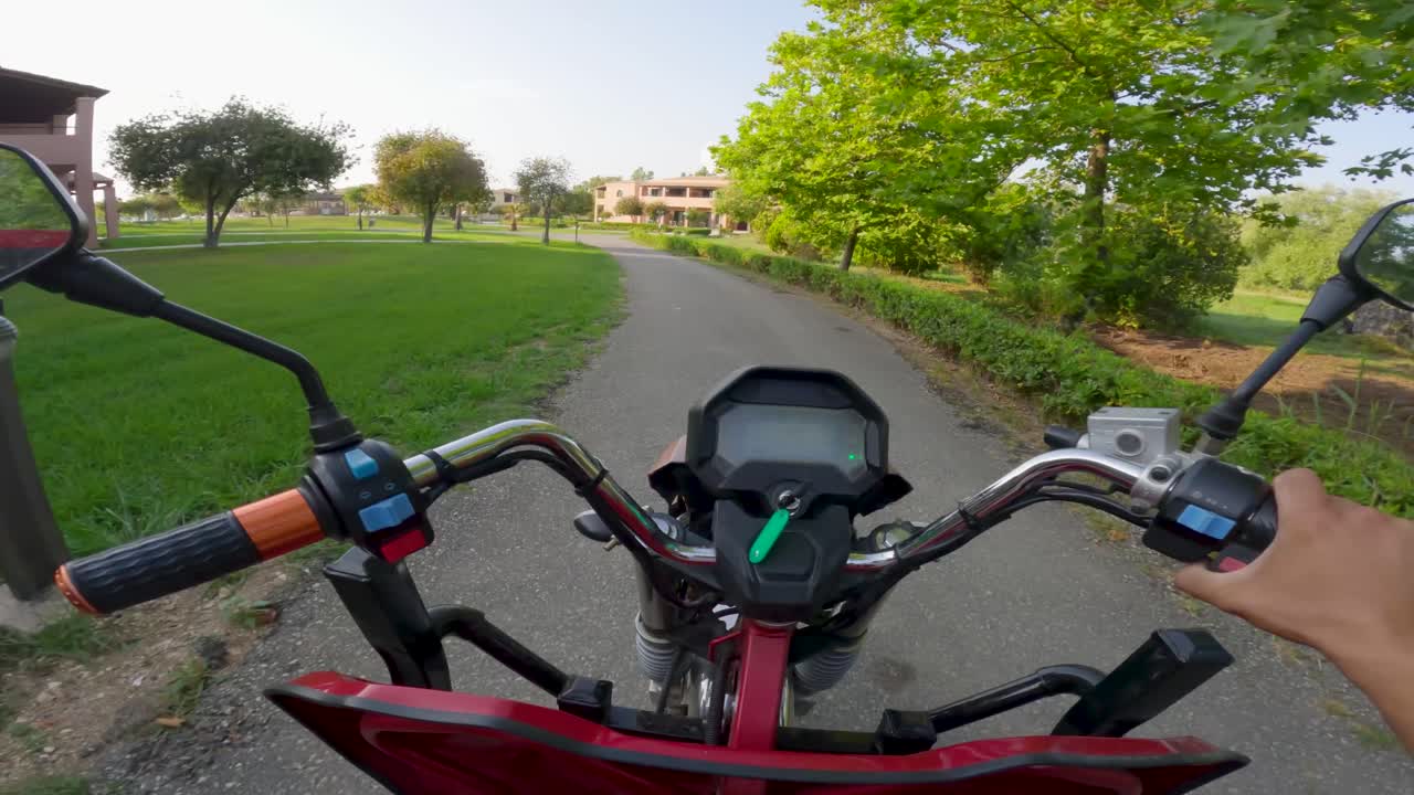 POV alla guida di un quad ATV rosso su sentiero pavimentato in uno splendido giardino verde estivo con alberi