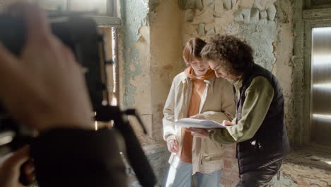 coworkers reading a script in a ruined building while they are being recorded by a cameraman 1