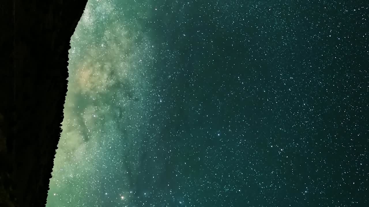 el núcleo de la vía láctea ascendiendo por encima del paisaje en silueta - lapso de tiempo vertical