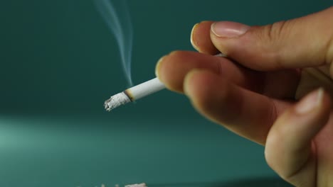 Closeup-shot-of-a-hand-holding-a-lit-cigarette,-with-smoke-trailing-from-the-cigarette,-stop-smoking-message