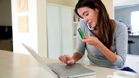 pretty brunette using laptop to shop online while talking on phone