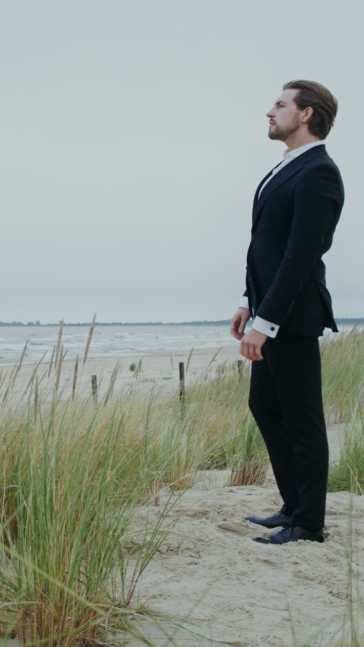 A formally dressed man standing on a beach