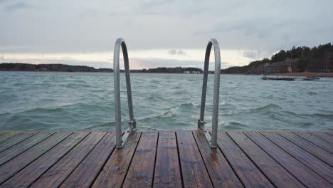 waves rocking a small wooden pier on a cloudy day