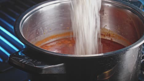 Ingredients,-white-rice-and-cabbage,-poured-into-soup-in-stainless-steel-pot-and-stirred-by-wooden-spoon