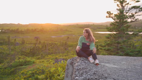 Mujer-Sentada-Sobre-Rocas-En-El-Desierto-En-Hora-Dorada-Puesta-De-Sol-Sonriendo