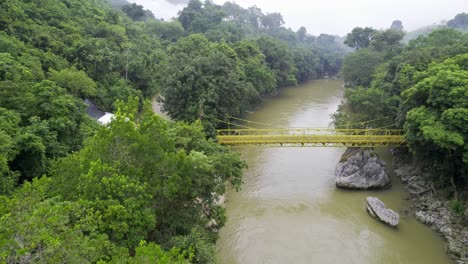 Drone-aerial-footage-of-yellow-bridge-over-river-Rio-Cahabon-near-Semuc-Champey-National-Park-in-Guatemala-surrounded-by-bright-green-rainforest-trees-near-Chicanutz