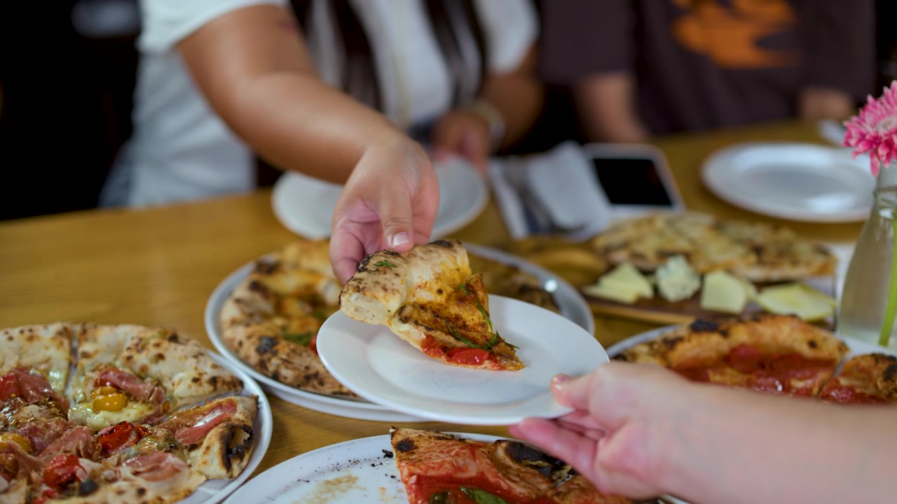 Primo piano di mani che servono una fetta di pizza gourmet su un piatto durante il pranzo.