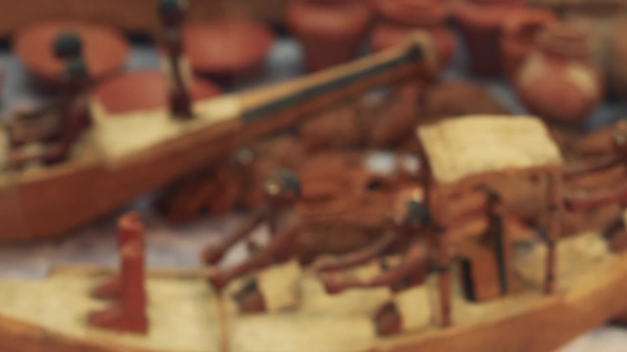 Close-up of miniature Egyptian boat with rowers and pottery in background.