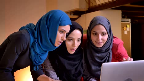 retrato en primer plano de tres mujeres de negocios musulmanas alegres usando la computadora portátil y emocionándose y alegrándose celebrando con alegría en el interior en el lugar de trabajo
