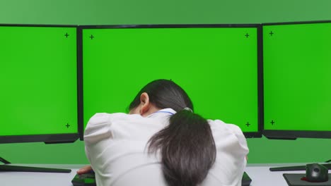 person leaning on computer desk with green screen monitors