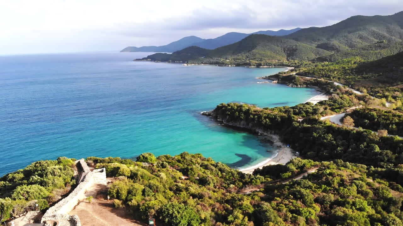 Hills covered with lush greenery. Remains of ancient structures on the top on the hill. Aegean sea coast. Road. Greece