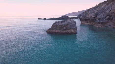 Aerial-4K-counterclockwise-orbit-and-crane-down-drone-shot-of-a-big-rock-in-the-crystal-clear-waters-of-the-sea-in-Greece-pt