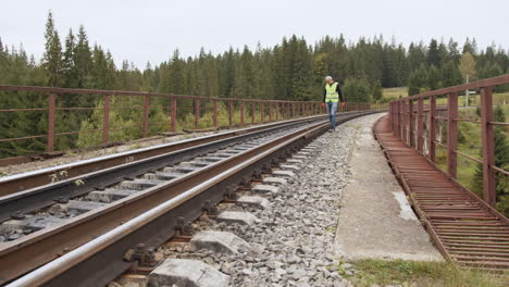 man walking on railroad tracks over a bridge in a forest