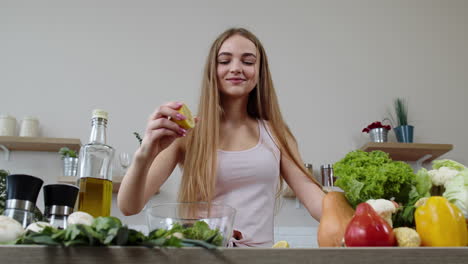 chica vegana cocinando ensalada con verduras crudas, añadiendo jugo de limón. exprimir una fruta de limón en las manos