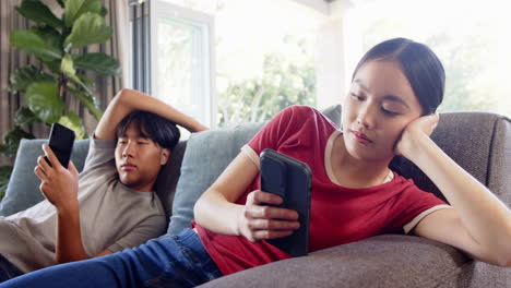 relaxing on couch, asian brother and sister using smartphones in living room