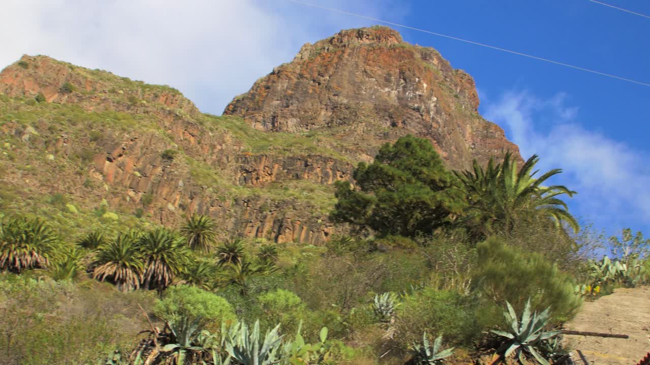 paisaje de montaña verde, cerca del pueblo de asentamiento remoto de la garganta de masca, acantilados escarpados, barranco, palmeras, nubes bajas que se mueven sobre las cimas de las colinas, tenerife, islas canarias, españa, toma panorámica de mano