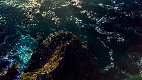 Tilting-down-view-of-rocky-cliffs-and-foaming-ocean-waves-at-sunset-in-Big-Sur-California