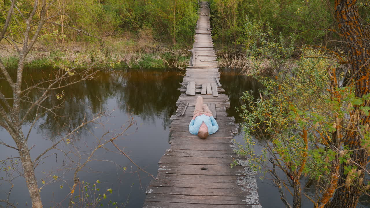 hombre relajándose en un puente de madera sobre un río en un bosque