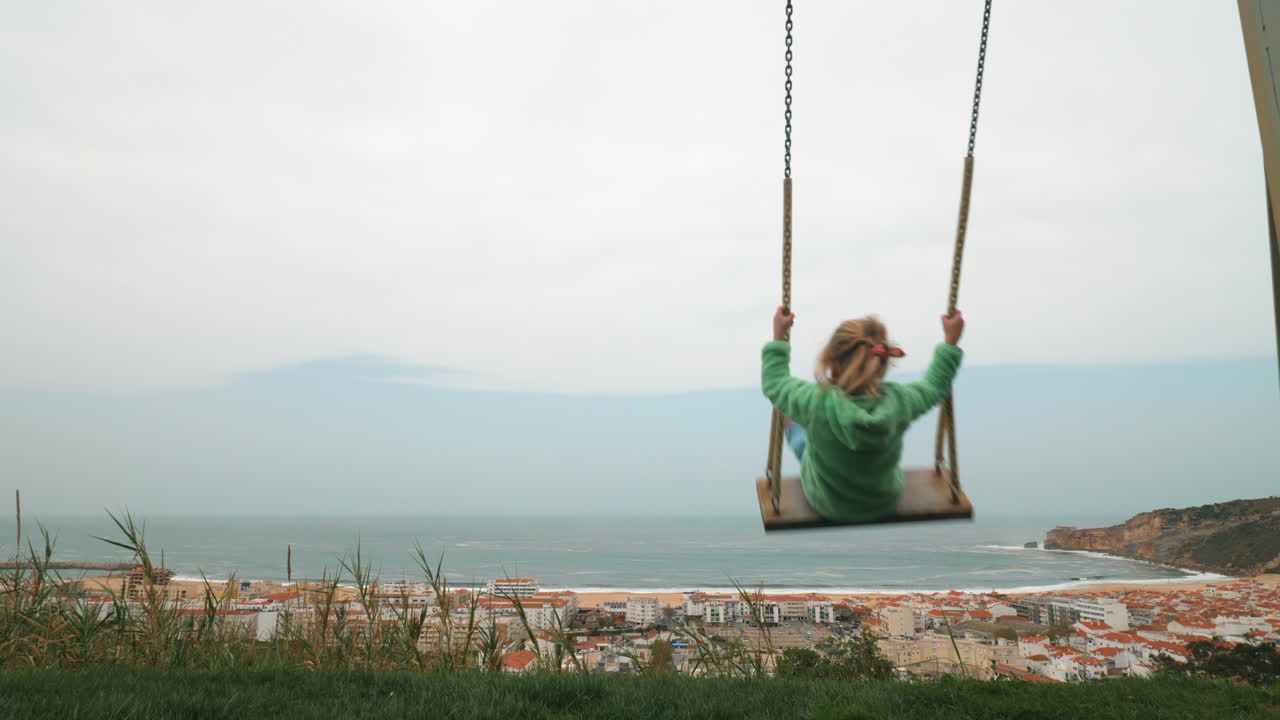 niña balanceándose contra la escena de la costa de nazare en portugal