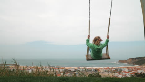 little girl swinging against the scene of nazare coast in portugal