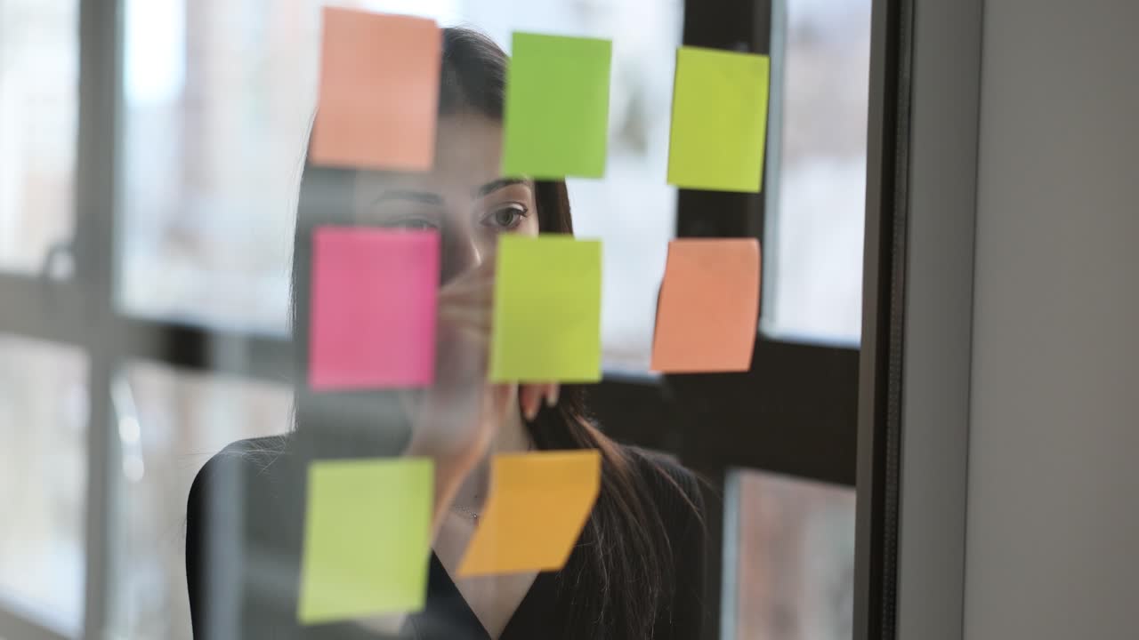 Una donna scrive su post-it un importante piano di lavoro su una lavagna di vetro
