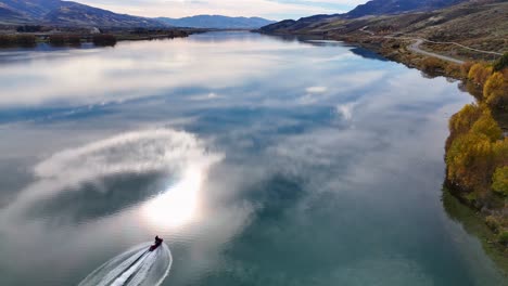 a jetski glides across lake dunstan, reflecting autumn colors and mountains, creating a serene and dynamic scene