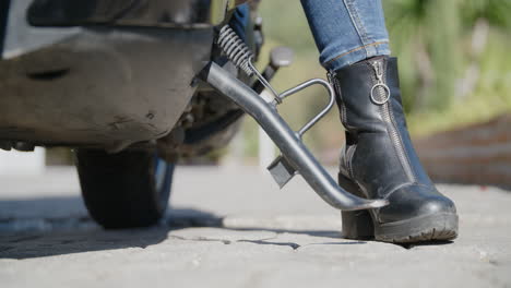 Primer-Plano-De-La-Bota-Negra-De-Mujer-Empujando-El-Scooter-Fuera-Del-Soporte