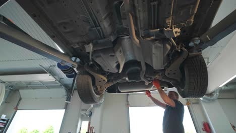 young professional mechanic man working under lifted modern car in auto repair service. car service, repair maintenance.