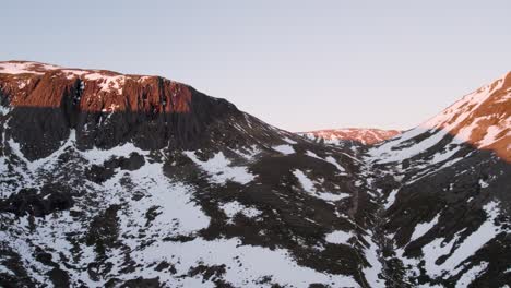 imágenes aéreas de drones panorámicos para revelar montañas y acantilados escarpados y dramáticos en un paisaje invernal con nieve, rocas y rocas al amanecer en una parte remota del parque nacional de cairngorms, escocia