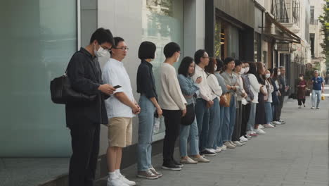 a line of people waiting on a city sidewalk