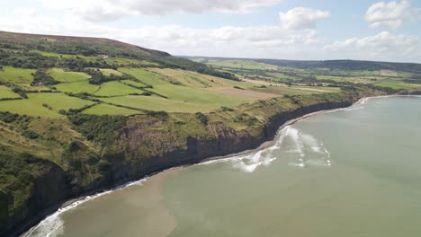 Aerial-drone-panning-shot-of-North-Yorkshire-coastline,-Ravenscar-with-green-fields-and-ocean