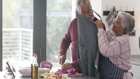 pareja biracial mayor usando delantales y cortando verduras en la cocina, sin alterar, en cámara lenta