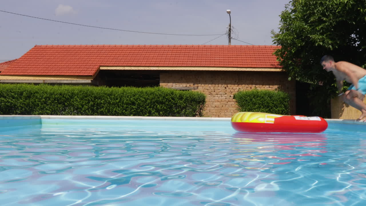 hombre saltando en una cama inflable en la piscina de la villa en un día caluroso, vista estática