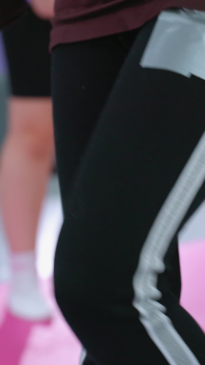 niño joven con gafas estirando el brazo mientras se equilibra en una pierna y trayendo la pierna hacia adelante en una postura enfocada, con vista parcial de otro niño realizando un movimiento similar en un gimnasio brillante